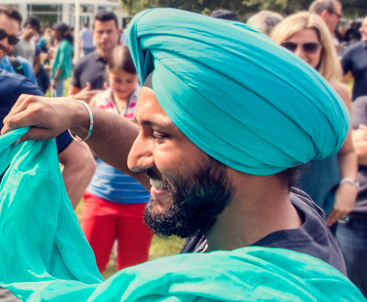Foto de um homem sorrindo com um turbante enquanto enrola um turbante em outra pessoa.