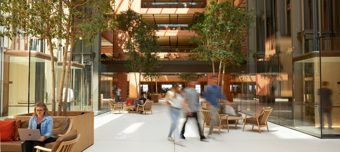 Das Erdgeschoss des lichtdurchfluteten Battersea Atriums mit vielen Apple Teammitgliedern, die sich treffen, durch das Atrium gehen oder auf verschiedenen Sitzgelegenheiten zusammenarbeiten.