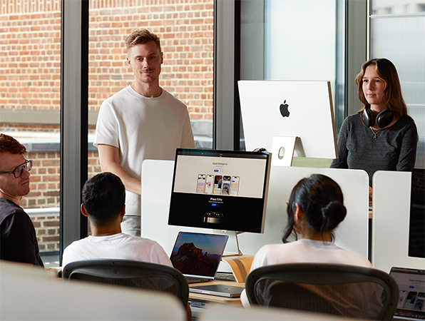 Fünf Apple Teammitglieder sind um ihre Tische herum versammelt und unterhalten sich.