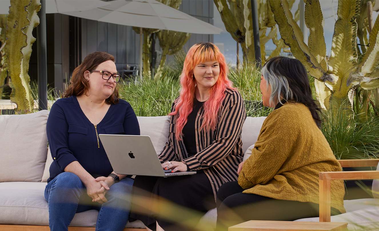 Tres empleadas de Apple, una de ellas con un MacBook, sentadas en un patio exterior.