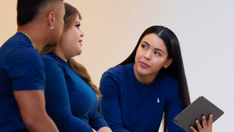 Drei Apple Retail Mitarbeiter:innen reden miteinander. Eine von ihnen hält ein iPad in der Hand.
