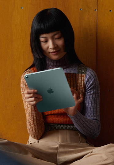 Une étudiante est assise sur le sol contre un mur et tient un iPad.