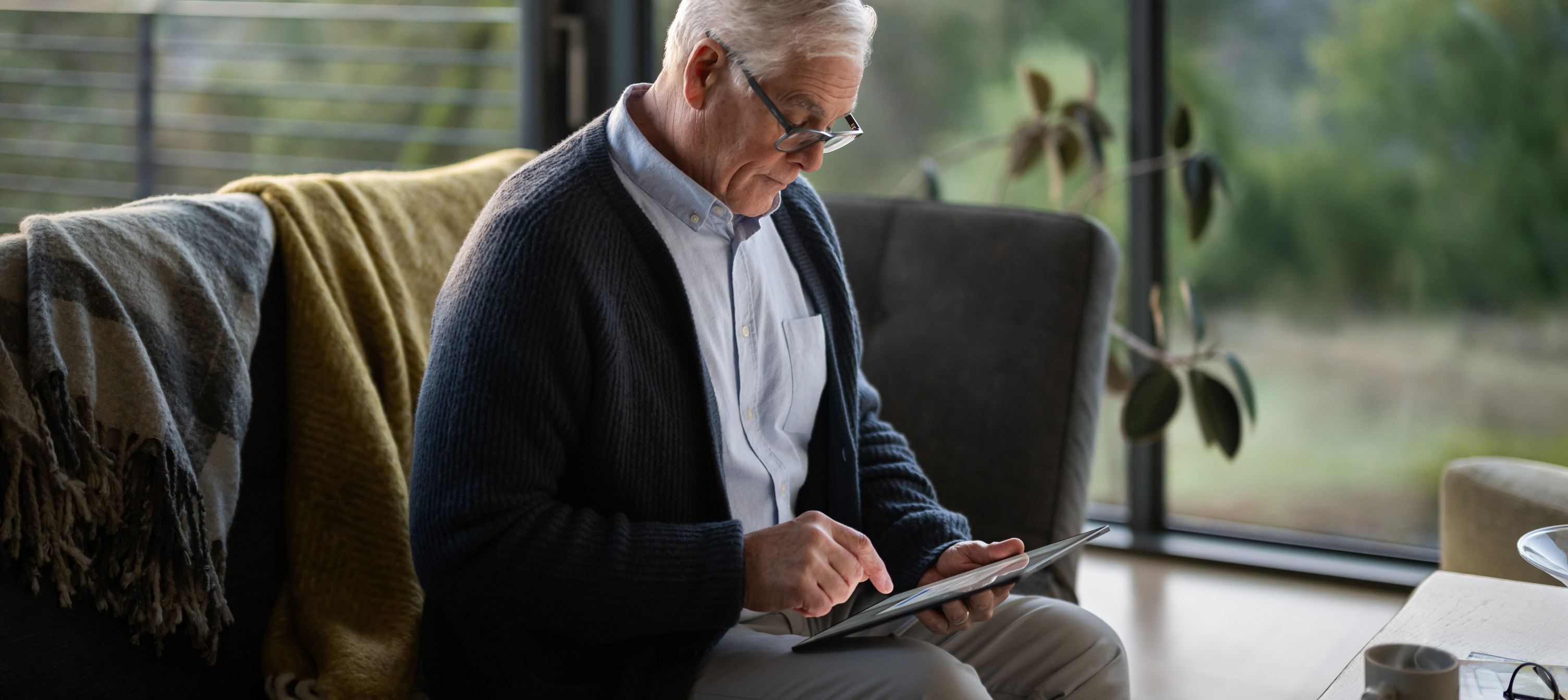 An elderly man sitting on a sofa looking at an iPad.