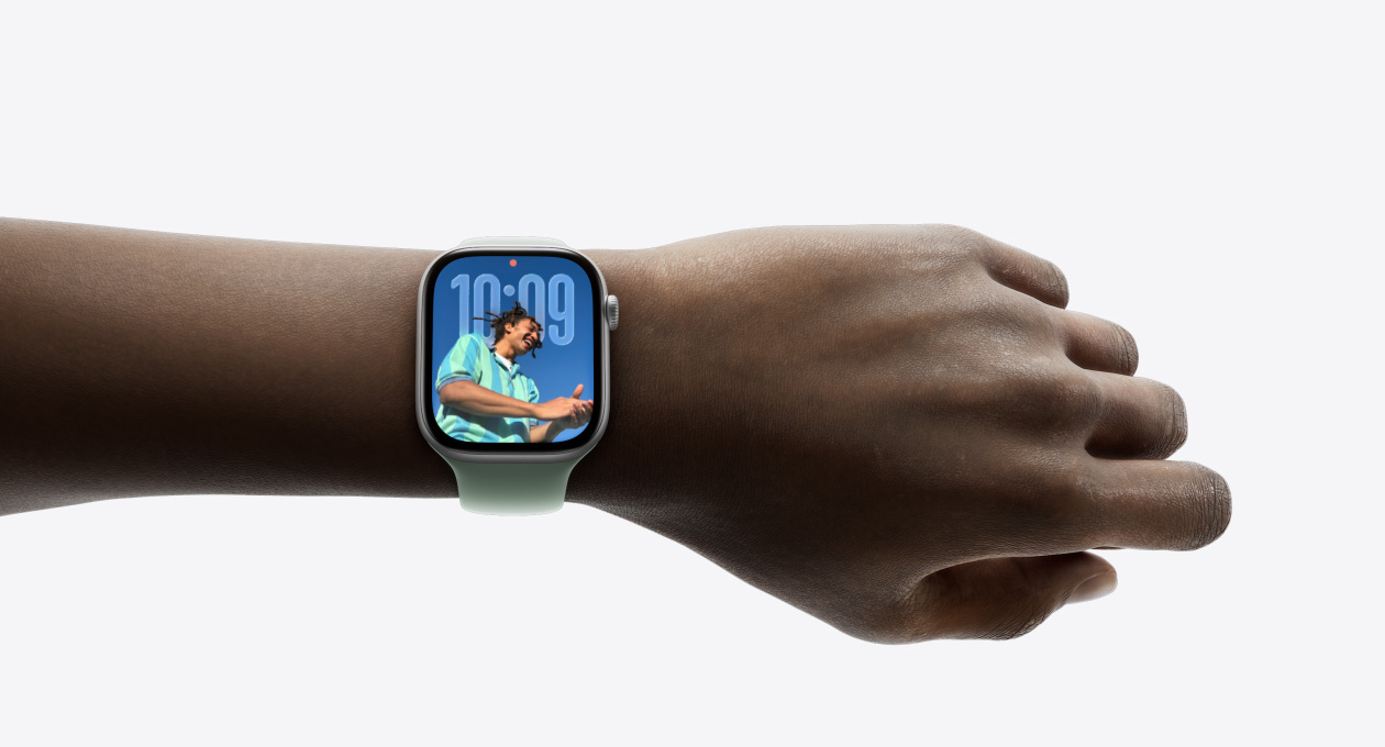 Primer plano de la muñeca de una persona con un Apple Watch en color plata y correa de goma, en cuya pantalla se puede apreciar el nuevo diseño con Liquid Glass